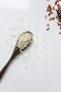 Top view of uncooked white and red rice grains in a wooden spoon on a white background, showcasing natural food.